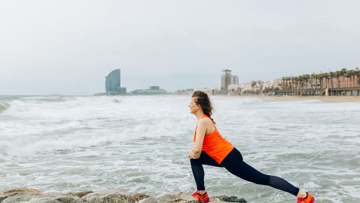 A woman stretches by the ocean in Barcelona, showcasing health and fitness by the sea.